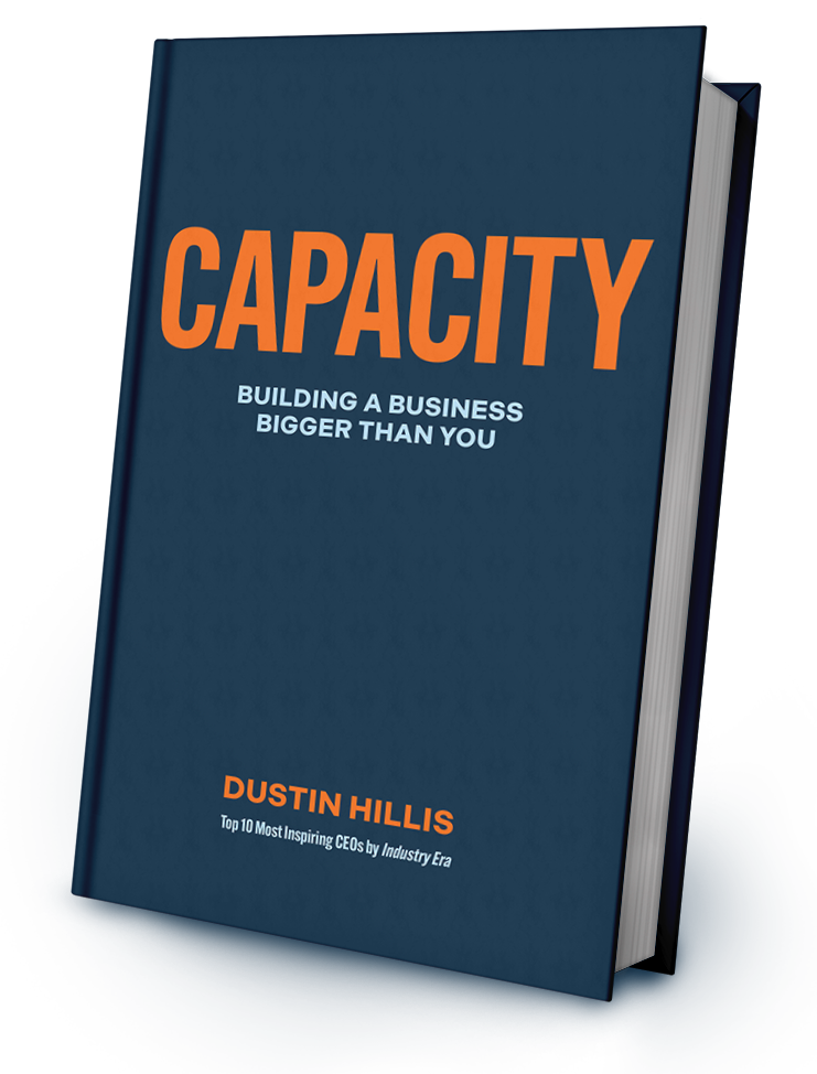 A dark blue hardcover book titled "CAPACITY: Building a Business Bigger Than You" by Dustin Hillis.